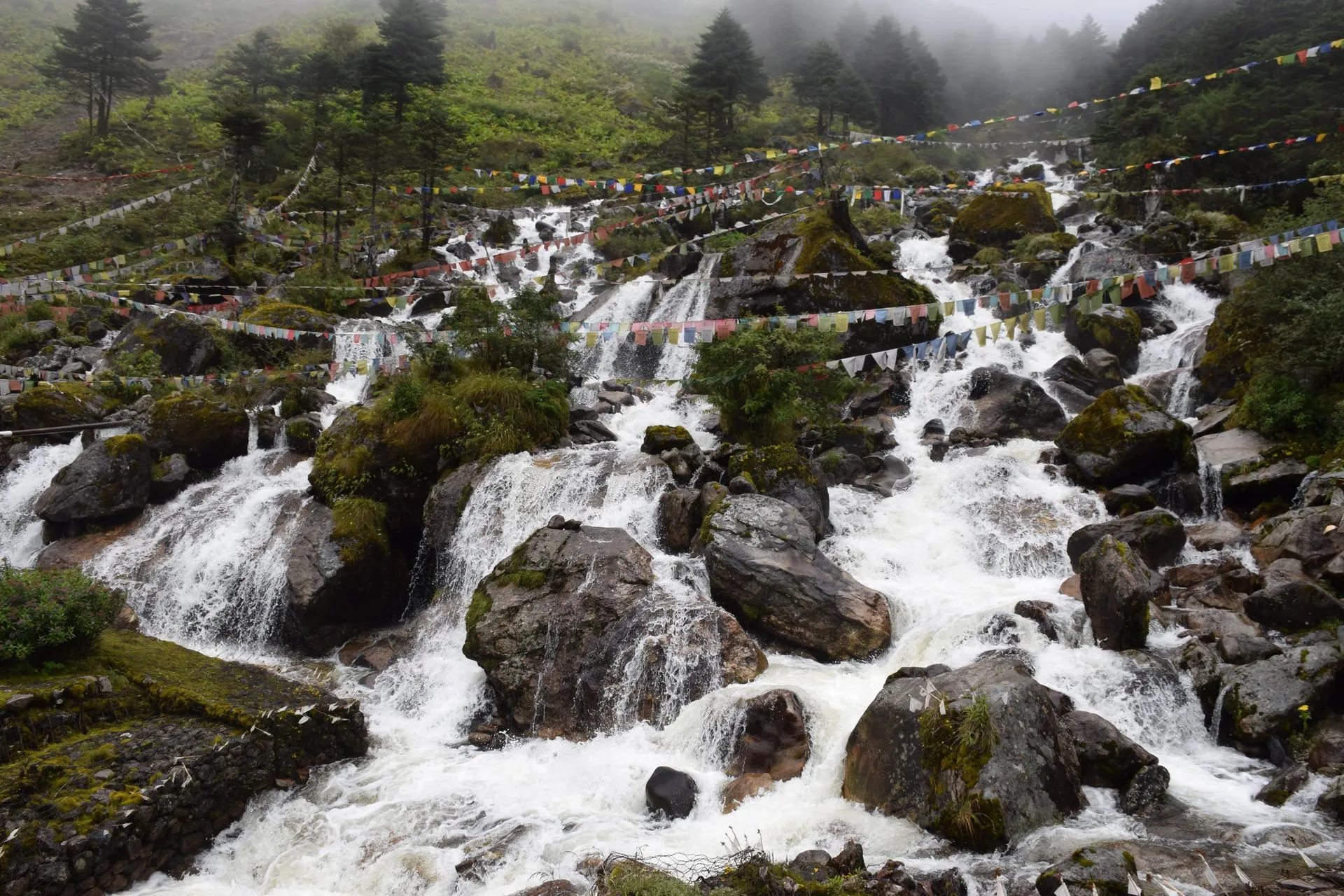Prayer flags beside a clear mountain stream on a route near Tawang